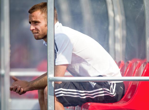 Ein Mann in Sportkleidung sitzt auf der Bank und blickt nachdenklich zur Seite.