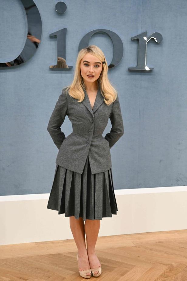 Sabrina Carpenter posiert vor dem Dior-Schriftzug in einem grauen Kostüm.