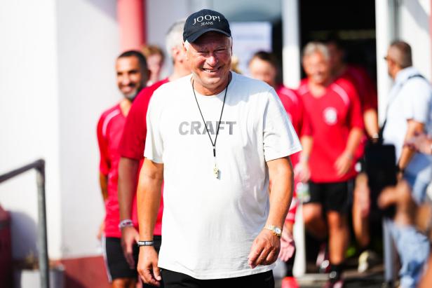 Ein lächelnder Mann mit Joop!-Kappe und Craft-T-Shirt führt eine Gruppe von Fußballspielern an.