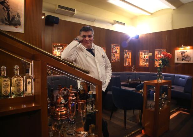 Heinz Kaiser posiert in einer Bar mit Spirituosenregalen.