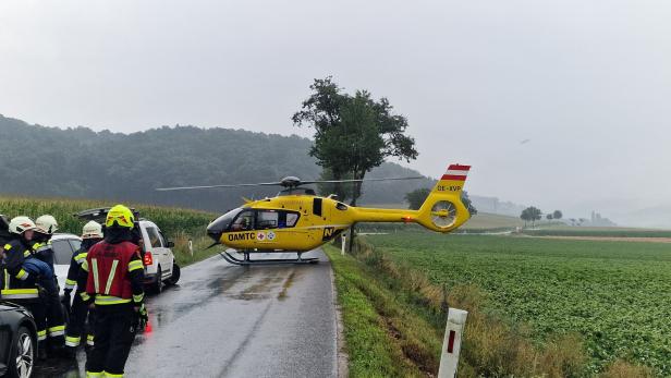 Ein gelber ÖAMTC-Rettungshubschrauber landet auf einer regnerischen Landstraße.