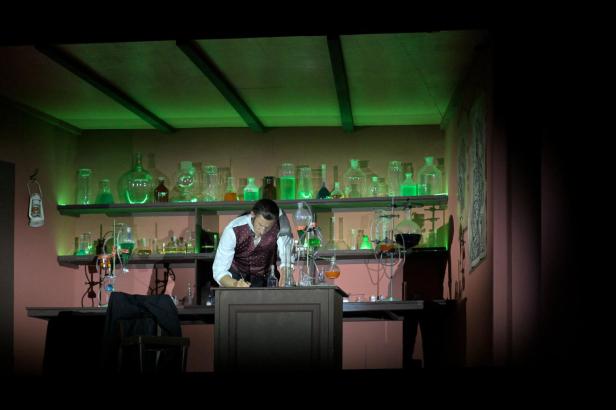 Ein Mann im Labor notiert etwas; im Hintergrund Reagenzgläser und Flaschen.