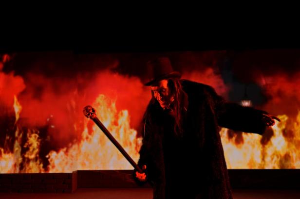 Ein Mann im Jekyll & Hyde-Kostüm steht vor einer Feuerkulisse.