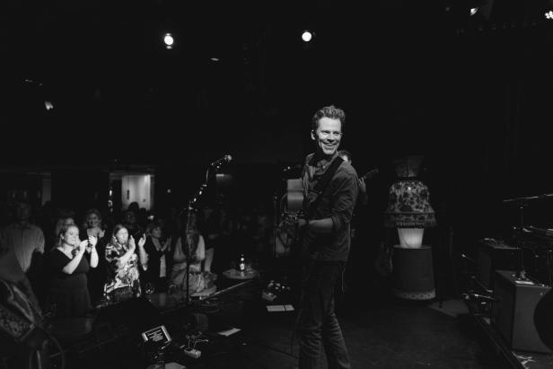Der Musiker mit Gitarre in der Hand, unten stehen die Fans.
