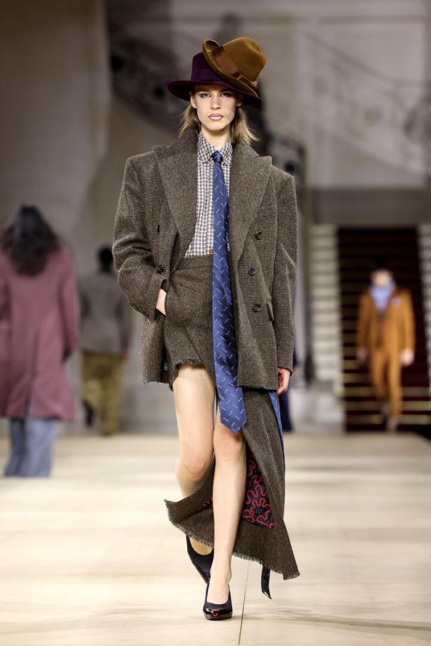 Ein Model auf dem Laufsteg trägt einen Tweed-Blazer, einen Minirock und zwei Hüte übereinander.