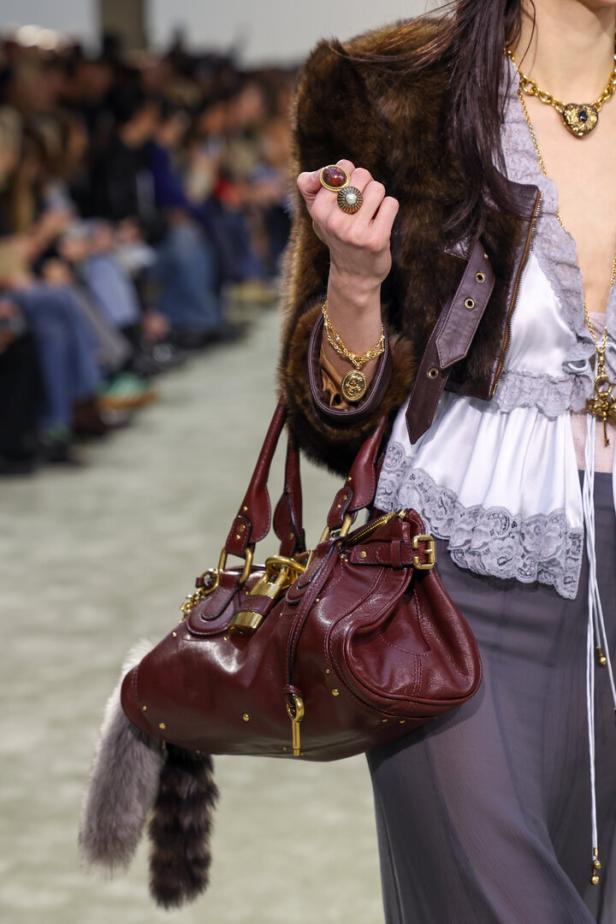 Eine Frau mit Schmuck und einer bordeauxroten Chloé-Handtasche auf dem Laufsteg der Pariser Fashion Week Herbst/Winter 2025-2026.