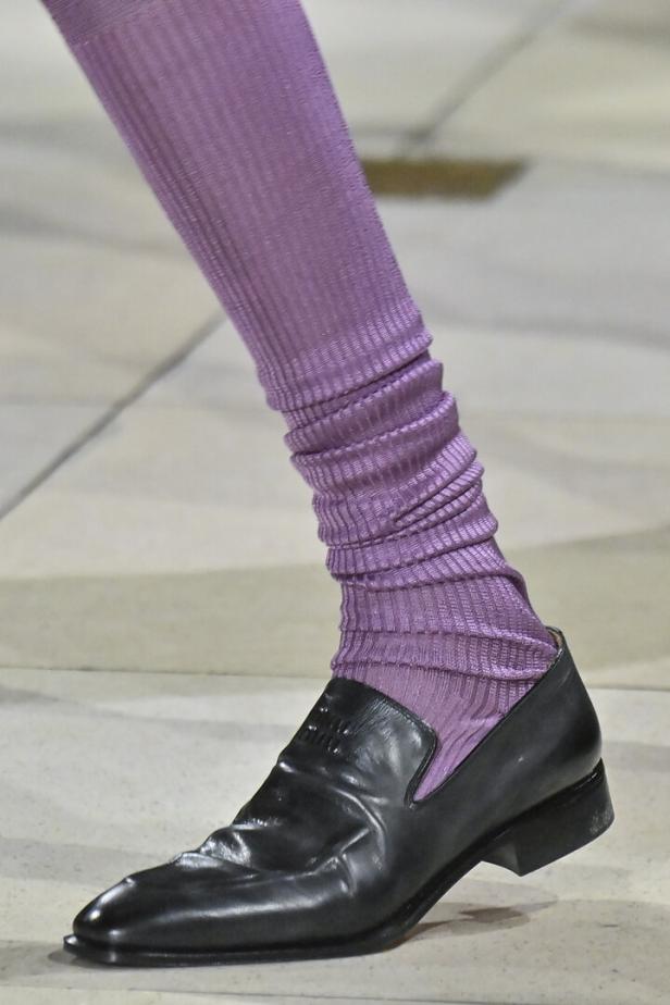 Ein Bein mit einer gerippten, lila Leggings und einem schwarzen Lederschuh von Miu Miu.
