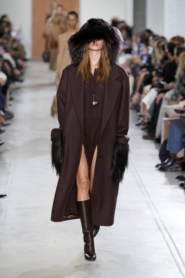 Eine Frau in einem braunen Mantel mit Fellbesatz und Stiefeln auf dem Laufsteg der Michael Kors Herbst/Winter Kollektion 2025/26.