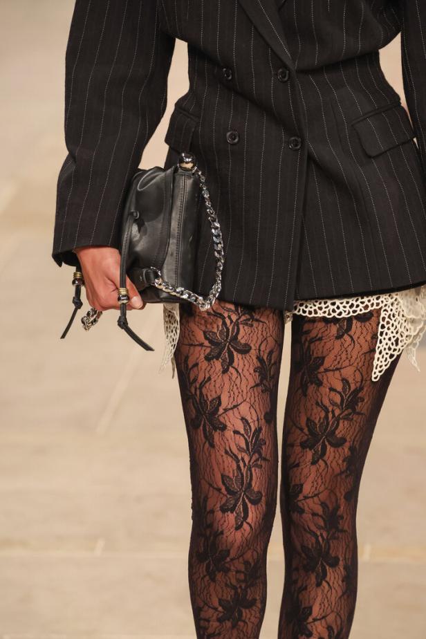 Detailaufnahme eines Models in einem gestreiften Blazer, floralen Strumpfhosen und einer schwarzen Handtasche bei der Isabel Marant Show.