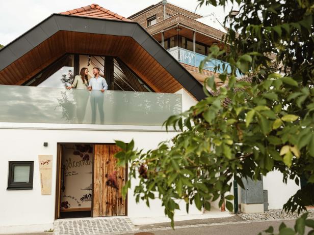 Ein renoviertes Holzhaus, auf dessen Balkon ein Paar steht 