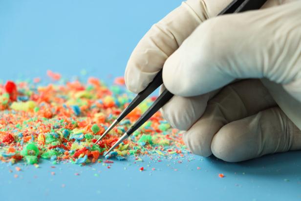 Close-up image of pile of multicoloured flakes and chips of plastic being sorted with tweezers held by unrecognisable person wearing medical gloves, blue background, focus on foreground, microplastics concept Close-up image of pile of multicoloured flakes and chips of plastic being sorted with tweezers held by unrecognisable person wearing medical gloves, blue background, focus on foreground, microplastics concept