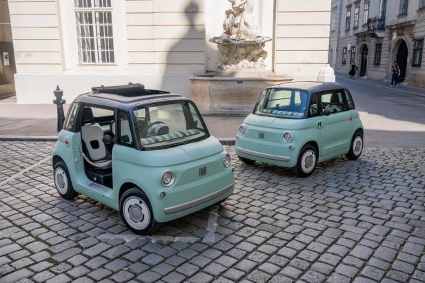 Zwei mintgrüne Fiat Topolino Elektroautos stehen auf einem gepflasterten Platz.