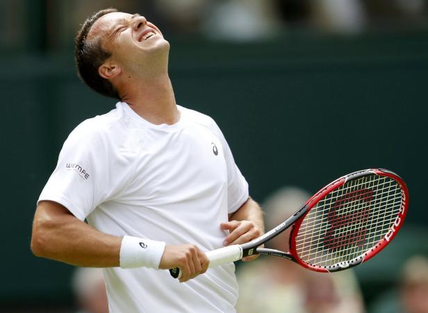 Ein Tennisspieler mit schmerzverzerrtem Gesicht hält einen Schläger in der Hand.