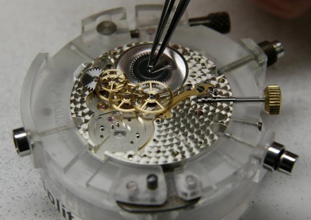 Employee works on watch plate by German watchmaker Eine Pinzette hantiert an den filigranen Zahnrädern eines Uhrwerks.