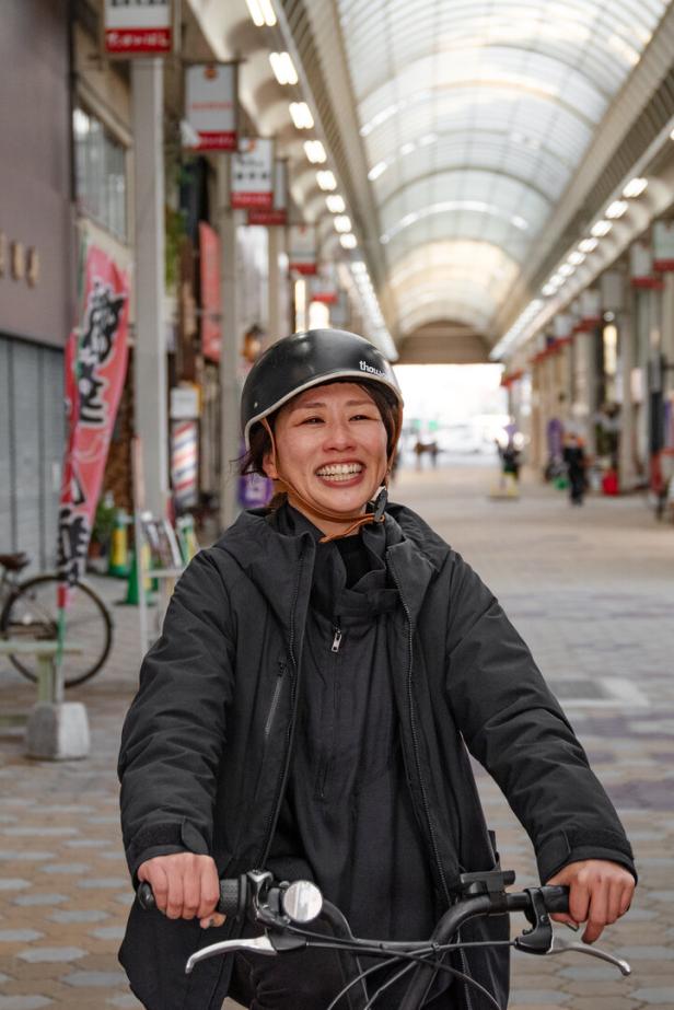 Eine lächelnde Frau fährt mit dem Fahrrad durch eine überdachte Ladenstraße.