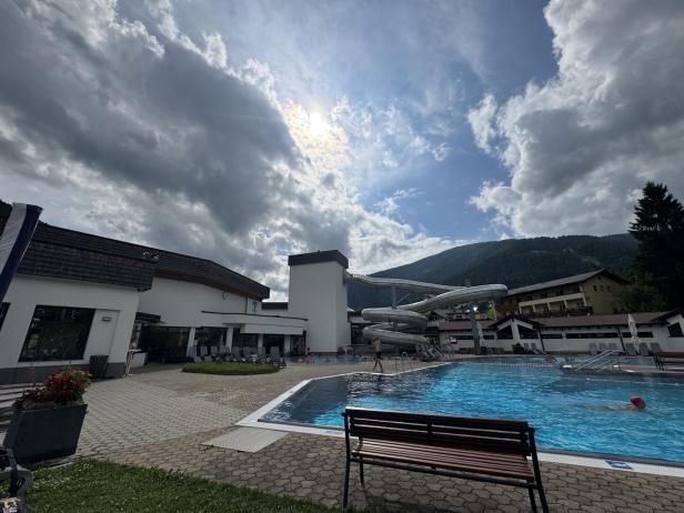Ein Freibad mit Wasserrutsche vor einer bewaldeten Bergkulisse.