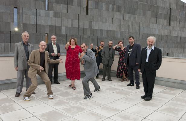 Eine Gruppe von zehn Personen posiert vor einer grauen Steinwand.
