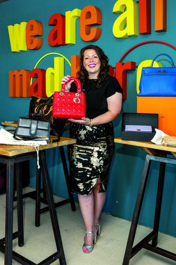 Eine Frau präsentiert eine rote „Lady Dior“-Handtasche vor einem farbenfrohen Hintergrund.