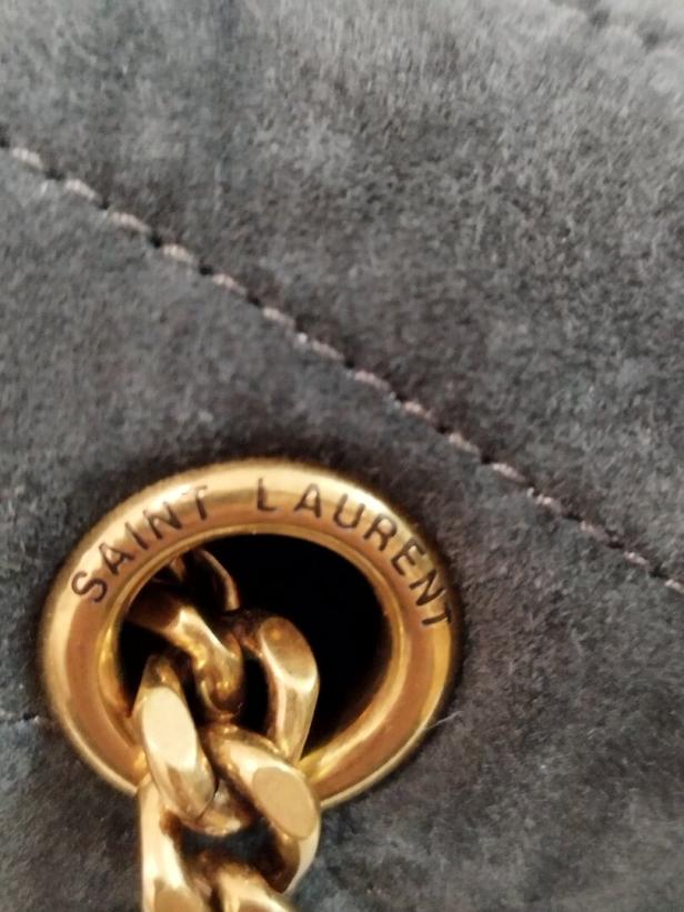 Detailaufnahme einer grauen Saint Laurent Tasche mit goldener Kette.