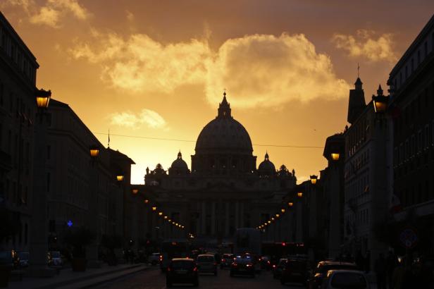 Der Petersdom in Rom bei Sonnenuntergang, gesehen von einer belebten Straße aus.