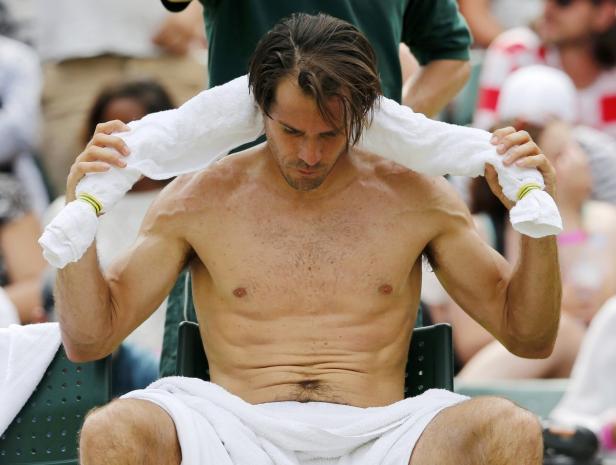 Ein Tennisspieler sitzt während einer Pause mit einem Handtuch um den Nacken auf einem Stuhl.