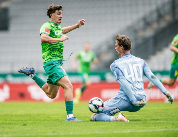 Ein Fußballspieler in Grün läuft auf einen Torwart zu, der auf dem Rasen kniet.