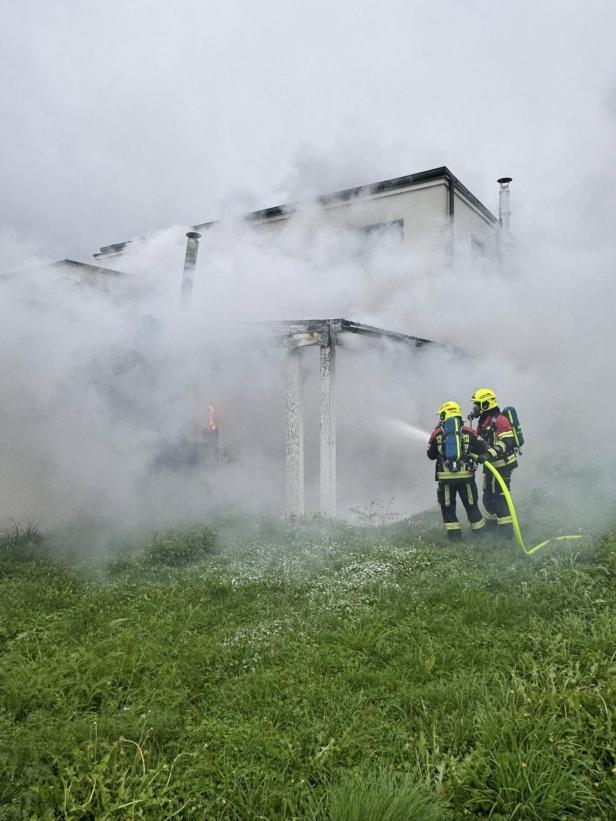 Zwei Feuerwehrleute bekämpfen einen Hausbrand mit einem Wasserstrahl.