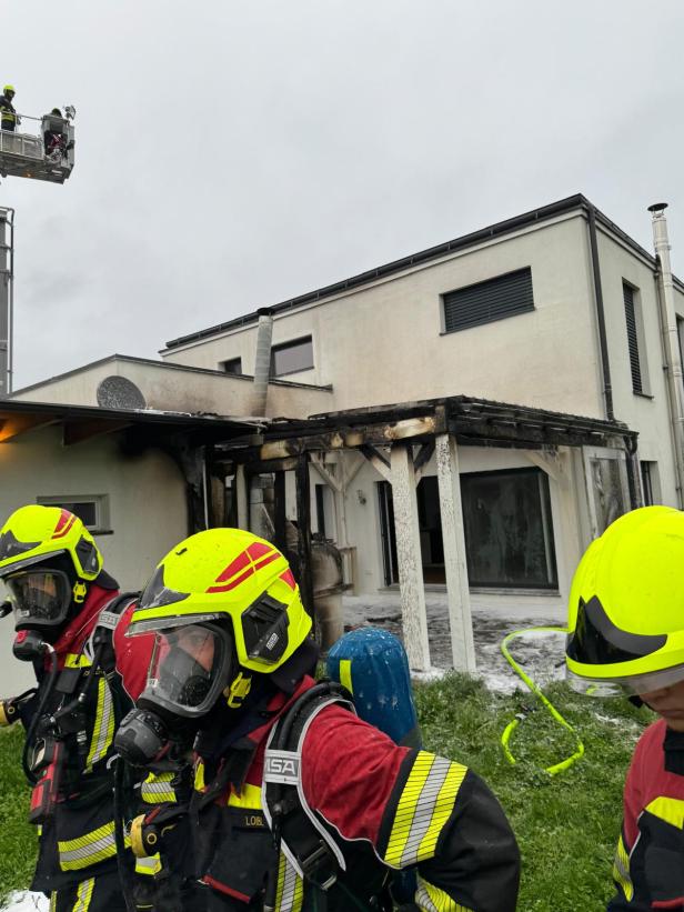 Feuerwehrleute stehen vor einem Haus mit Brandschaden.