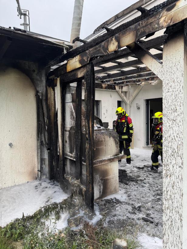 Zwei Feuerwehrleute stehen vor einem durch einen Brand beschädigten Gebäude.