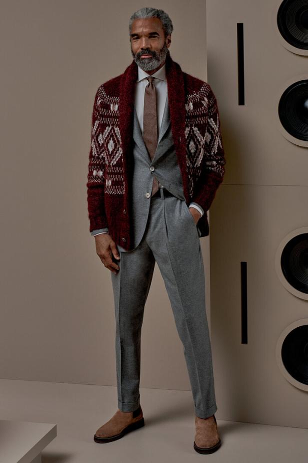 Ein Mann mit grauem Haar trägt einen grauen Anzug und eine rote Strickjacke.