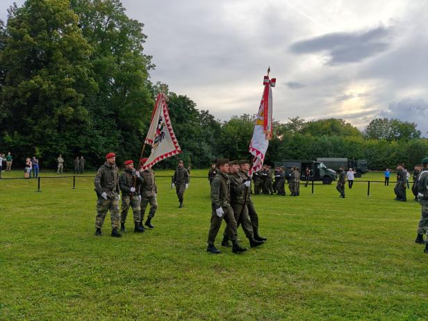 Soldaten marschieren bei der Angelobung in Großharras mit Fahnen.