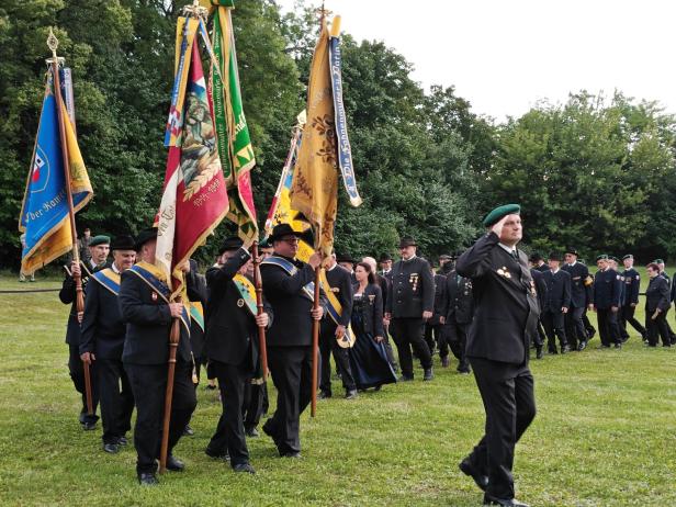 Eine Gruppe von Männern in Tracht marschiert mit Fahnen bei einer Angelobung in Großharras.