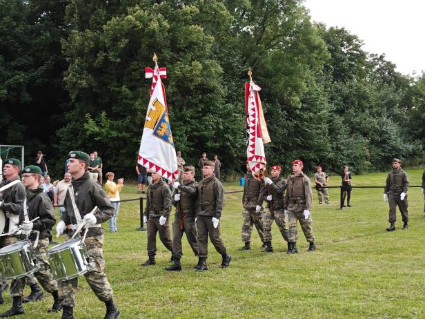 Soldaten marschieren bei der Angelobung in Großharras mit Fahnen.