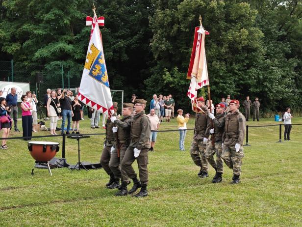 Soldaten marschieren bei der Angelobung in Großharras mit Fahnen auf einem Rasen.