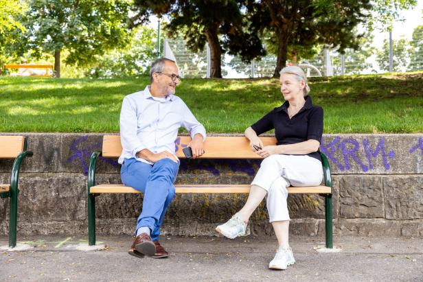 Marlene Streeruwitz sitzt mit einem Mann auf einer Bank im Park.