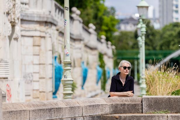 Eine Frau mit Sonnenbrille lehnt an einer Steinmauer in Wien.