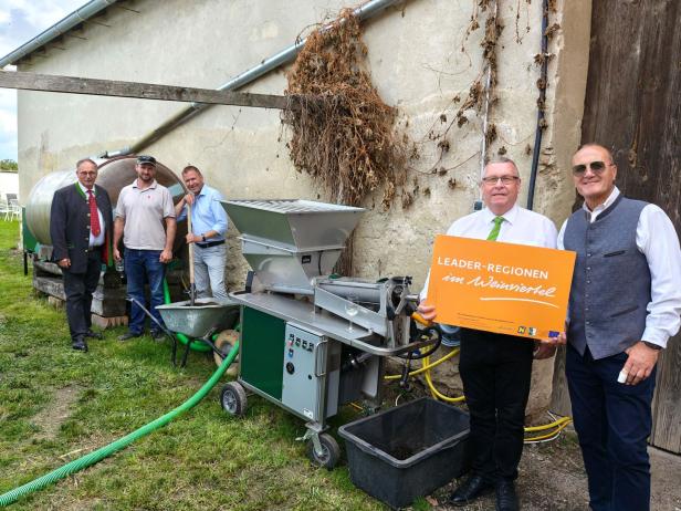 Eine Gruppe von Personen steht neben einer Weinpresse mit dem Schild „LEADER-Regionen im Weinviertel“.