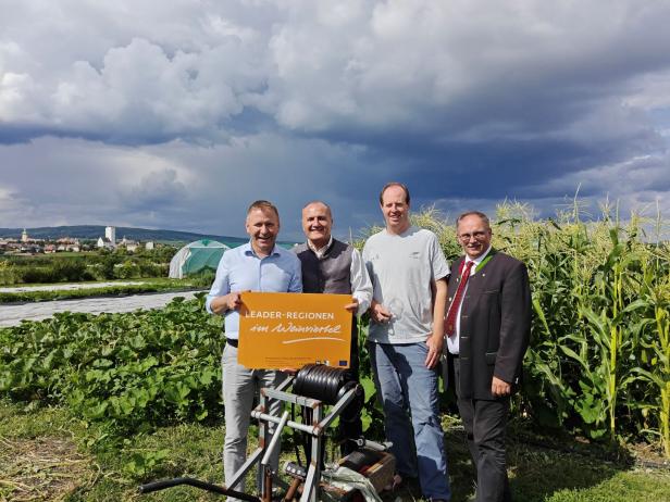 Vier Männer posieren mit einem Schild der Leader-Regionen im Weinviertel auf einem Feld.