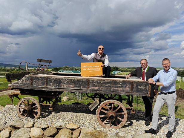 Drei Männer posieren auf einem alten Wagen mit einem Schild „LEADER-Regionen im Weinviertel“.