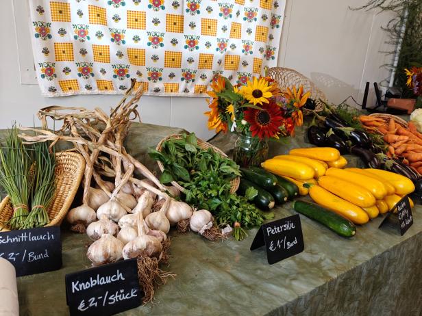 Verschiedene Gemüsesorten wie Knoblauch, Zucchini und Kräuter werden auf einem Tisch zum Verkauf angeboten.