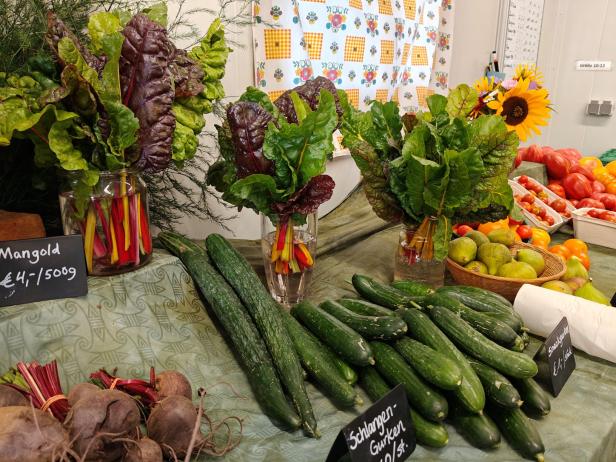 Ein Marktstand mit Mangold, Schlangengurken, Tomaten und Sonnenblumen.