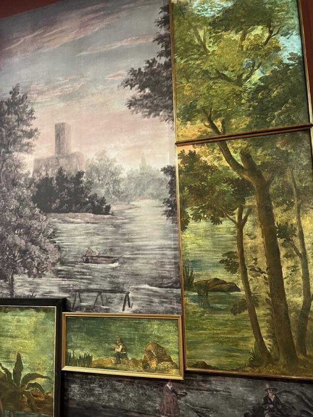 Eine Wand mit verschiedenen Landschaftsgemälden, darunter eine Szene mit einem Fluss und Bäumen.
