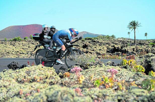 Ein Radfahrer nimmt am Ironman Lanzarote 2025 teil, begleitet von einem Motorrad.