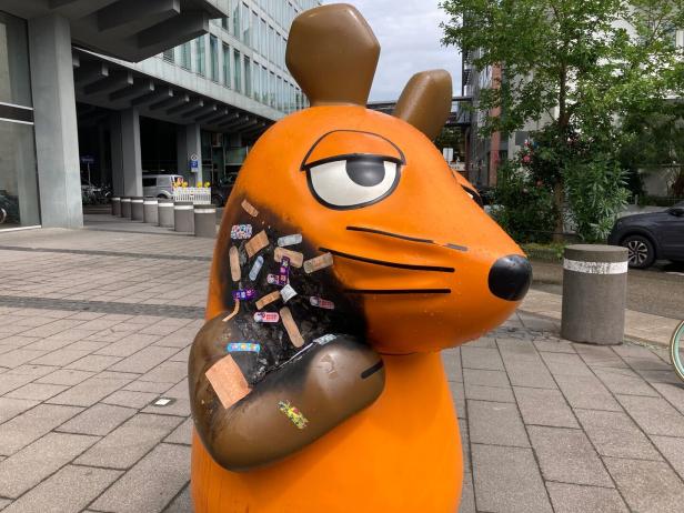 Pflaster für die Maus Eine orangefarbene Maus-Skulptur mit Pflastern auf dem Körper.