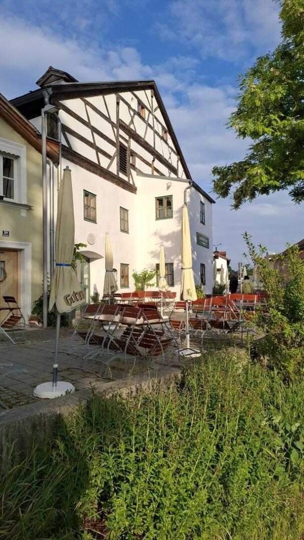 Ein Biergarten mit Tischen und Sonnenschirmen vor einem traditionellen Fachwerkhaus.