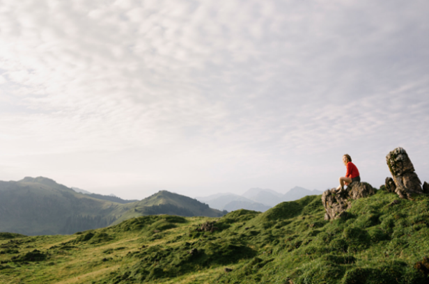 Eine Frau sitzt auf einem Felsen in den Bergen und genießt die Aussicht auf die umliegende Landschaft.