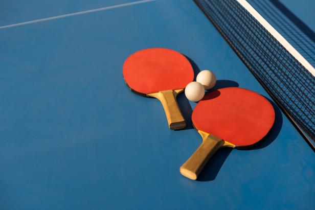 Table tennis ping pong paddles and white ball on blue board.
