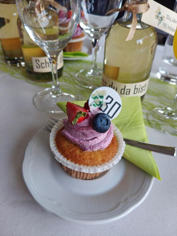 Ein Cupcake mit lila Frosting, Erdbeere, Blaubeere und einem „30“-Topper steht auf einem Tisch.