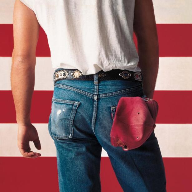 Ein Mann in Jeans und weißem T-Shirt steht vor einem rot-weiß gestreiften Hintergrund.