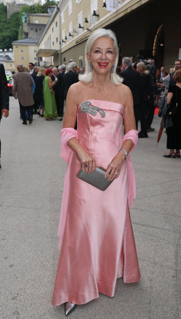 Eine ältere Frau in einem rosa Abendkleid und mit einer silbernen Clutch auf einer Veranstaltung.